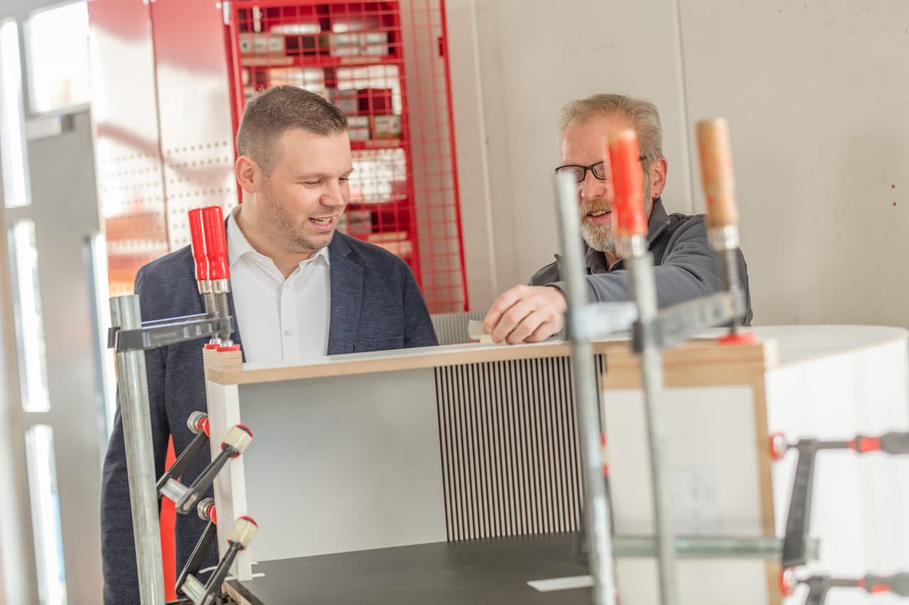 Simon Herbst bespricht mit einem Tischler ein Möbel in der Werkstatt in Springe